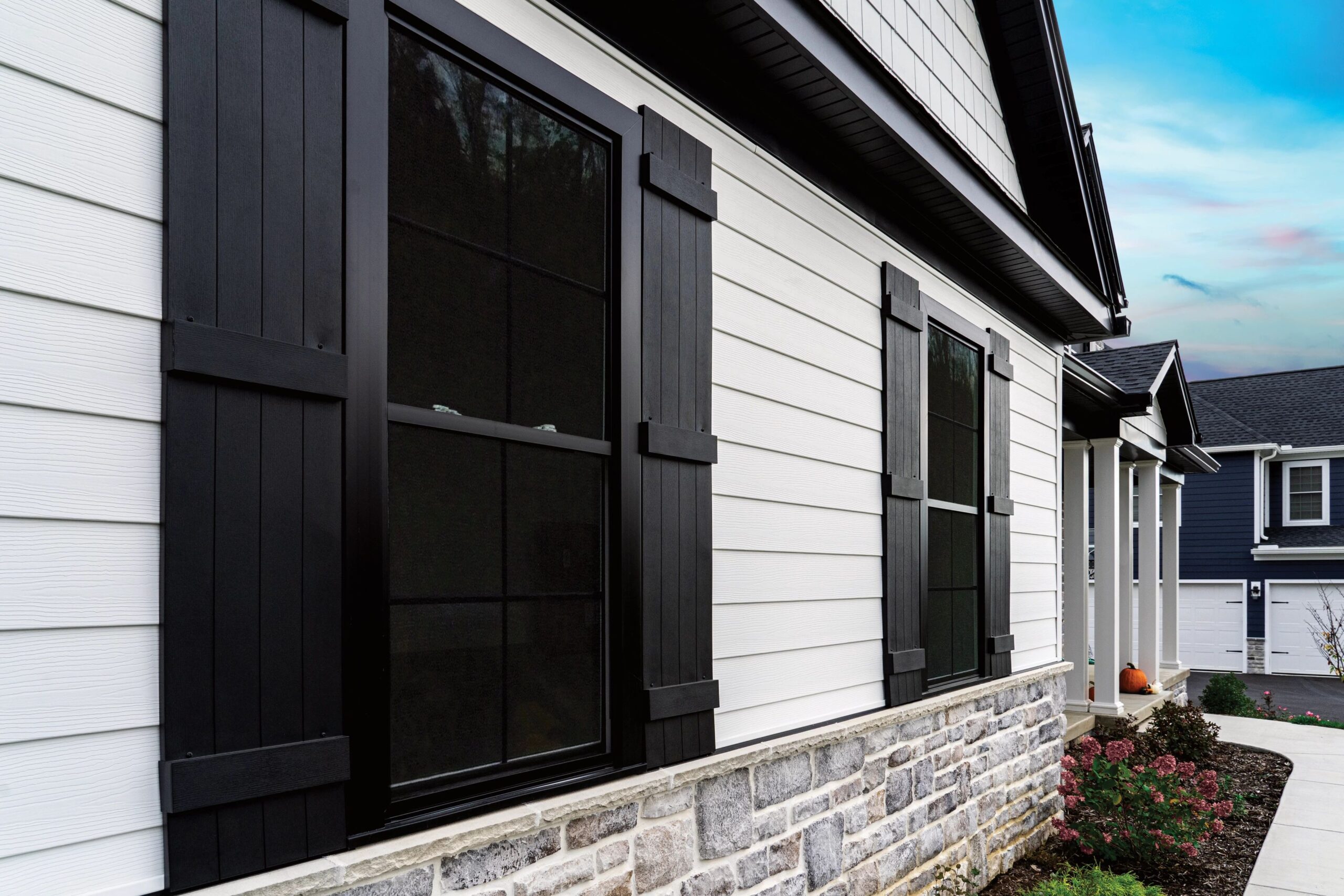 White horizontal siding with contrasting black shutters and stone accents